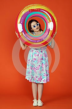 Woman standing looking at the side through colorful inflatable tube surprised face expression, isolated on orange