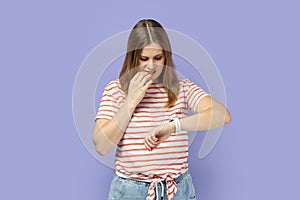 Woman standing looking at smartwatch and biting her nails, being stressed and worried.