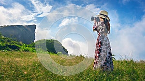 Woman standing on meadow and holding camera take photo at Phu Chi Fa mountains in Chiangrai, Thailand. Travel concept. photo