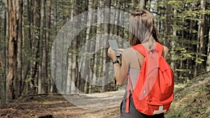 Woman standing in middle of forest, using navigation app on smartphone, following route with help of map, looking at