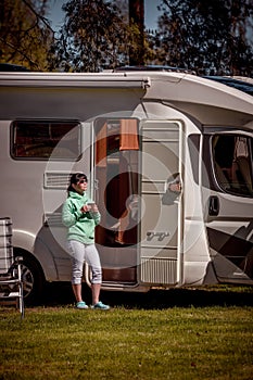 Woman is standing with a mug of coffee near the camper RV.