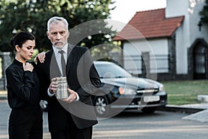 Woman standing near bearded man with mortuary urn