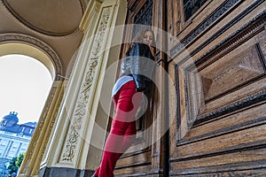 Woman is standing near big wooden door in old style building of the academy. Photography angle from below