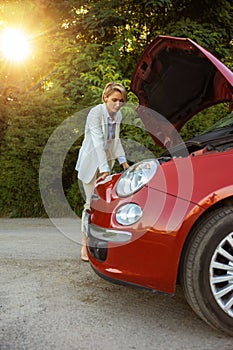 Woman standing near broken automobile on road waiting for service