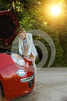 Woman standing near broken automobile on road waiting for service