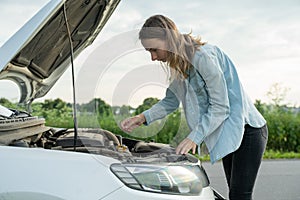 Woman standing near the broken car. The girl opened the hood and look at the engine.