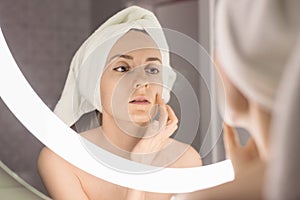 Woman standing near mirror in the bathroom and applying moisturizer her face