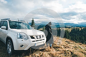Woman standing near suv car at hill peak looking at beautiful view of mountains