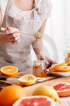 Woman standing near table with citruses and holding honey.