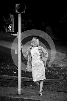 A woman standing near a traffic light at a crosswalk. Black and white photo.