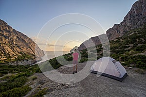 Woman standing near white tent in mountains watching sunrise over cap de formentor on Mallorca island, Spain