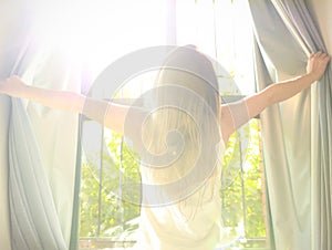 Woman standing near the window which  stretching near bed after waking up with sunrise at morning and lens flare