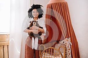 Woman standing near woven cradle and holding teddy bear