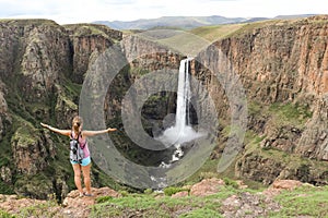 Woman standing next to stunning waterfall running down a steap canyon