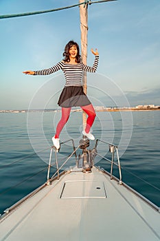 Woman standing on the nose of the yacht at a sunny summer day, breeze developing hair, beautiful sea on background