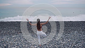 Woman is standing on one leg and meditating in front sea in daytime