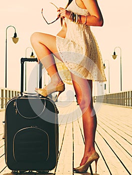 Woman standing one leg on suitcase, summertime