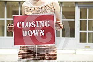 Woman Standing Outside Empty Shop Holding Closing Down Sign photo