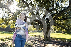 A woman is standing in a park, wearing a scarf and a white shirt