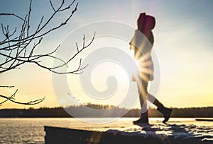 Woman standing on a pier by a lake in winter at sunset.