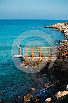 Woman standing on pier near rough stones and waving sea