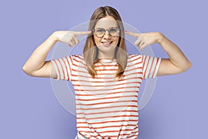 Woman standing and pointing at her spectacles, looking at camera with optimistic look.