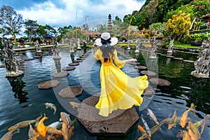 Woman standing in pond with colorful fish at Tirta Gangga Water Palace in Bali, Indonesia.