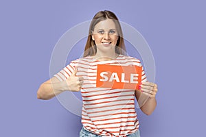 Woman standing with sale card in hands and showing thumb up, like gesture, like good discounts.