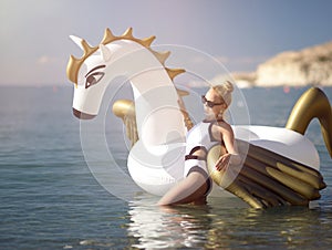 Woman standing on sea shore beach near resort hotel with giant inflatable unicorn pegasus float mattress in white bikini