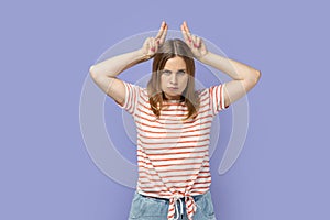 Woman standing and showing horns, being anger and aggressive, looking at camera.