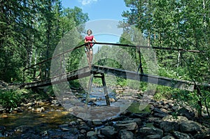 Woman standing on a  small bridge under mountain river in the forest