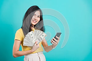 Woman standing smile holding money fan banknotes 100 dollar bills using mobile phone