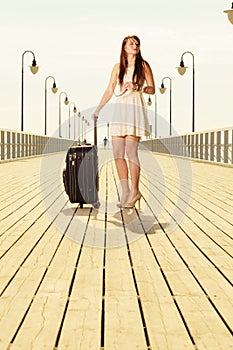 Woman standing with suitcase, pier in background