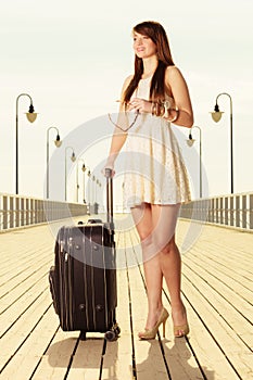 Woman standing with suitcase, pier in background