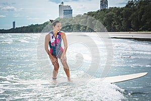 woman standing on a surfboard smiling happy from the surf which is exercise and activities that she enjoys