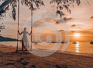 Woman standing on a swing on the beach in Thailand, Koh Tao watching sunset