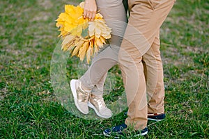 Woman is standing on tiptoe next to man, holding a wreath of yellow leaves in her hands. Legs close up