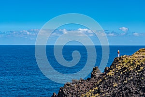 Woman standing on a top of a clif and enjoying the view to the Ocean at Sao Miguel, Azores