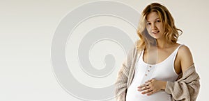 Woman standing and touching with hands her big belly. Isolated on gray background. Emotional loving pregnancy