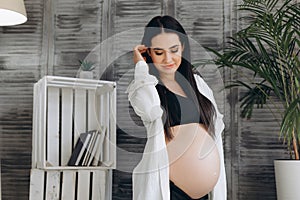 Woman standing and touching with hands her naked big belly.  on gray background. Emotional loving pregnancy time