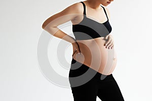 Woman standing and touching with hands her naked big belly. Isolated on gray background. Emotional loving