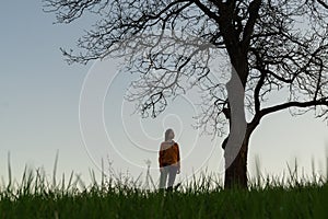 Žena stojaca pod orechom počas farebného západu slnka.