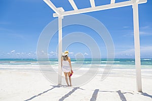 Woman standing under a white pergola looking out at a Beautiful Caribbean beach scene