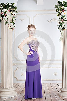 Woman standing in violet long dress nera column. Luxury interior