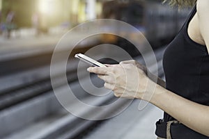 Woman standing and waiting for train and using smart phone in train station. Travel concept