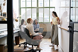 Woman standing at whiteboard in a meeting with female team