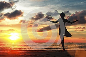 woman standing at yoga pose on beach during amazing sunset.