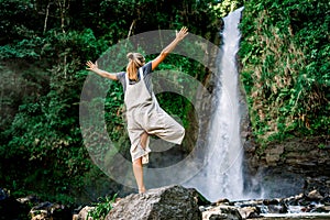 Woman standing in a yoga pose in front of a waterfall in the jungle