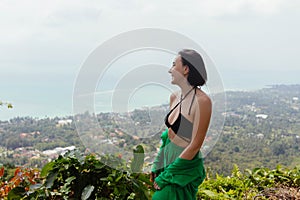 Woman stands admiring the view of a lush, coastal landscape from a high vantage point