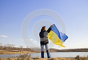 woman stands against the background of the lake and holds the Ukrainian yellow-blue flag against the sky